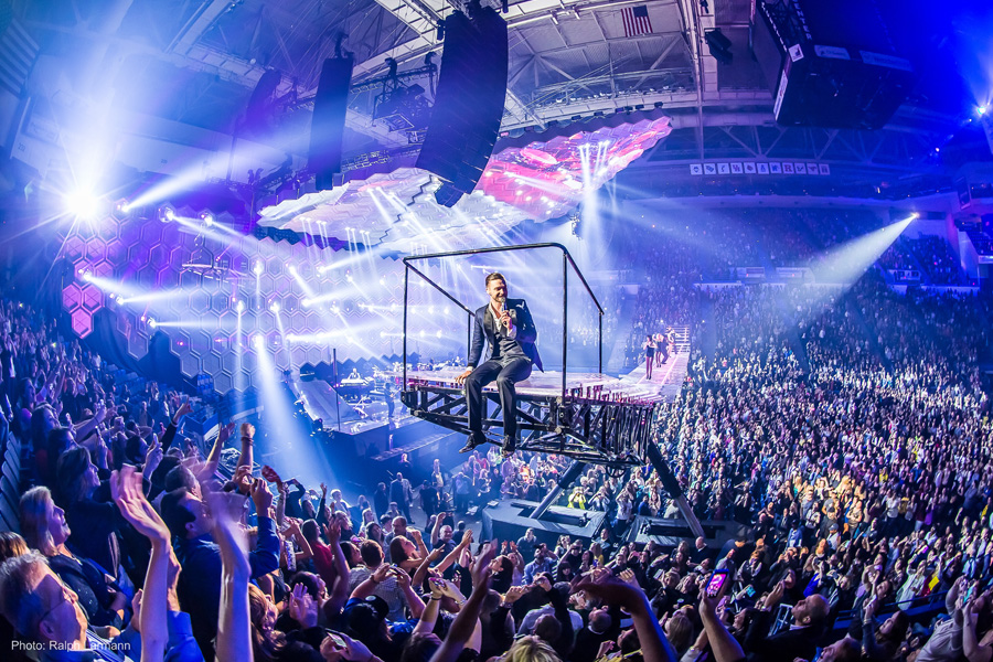 Concert staging at the XL Center. A performing is sitting on a raised platform over a crowd of cheering fans.