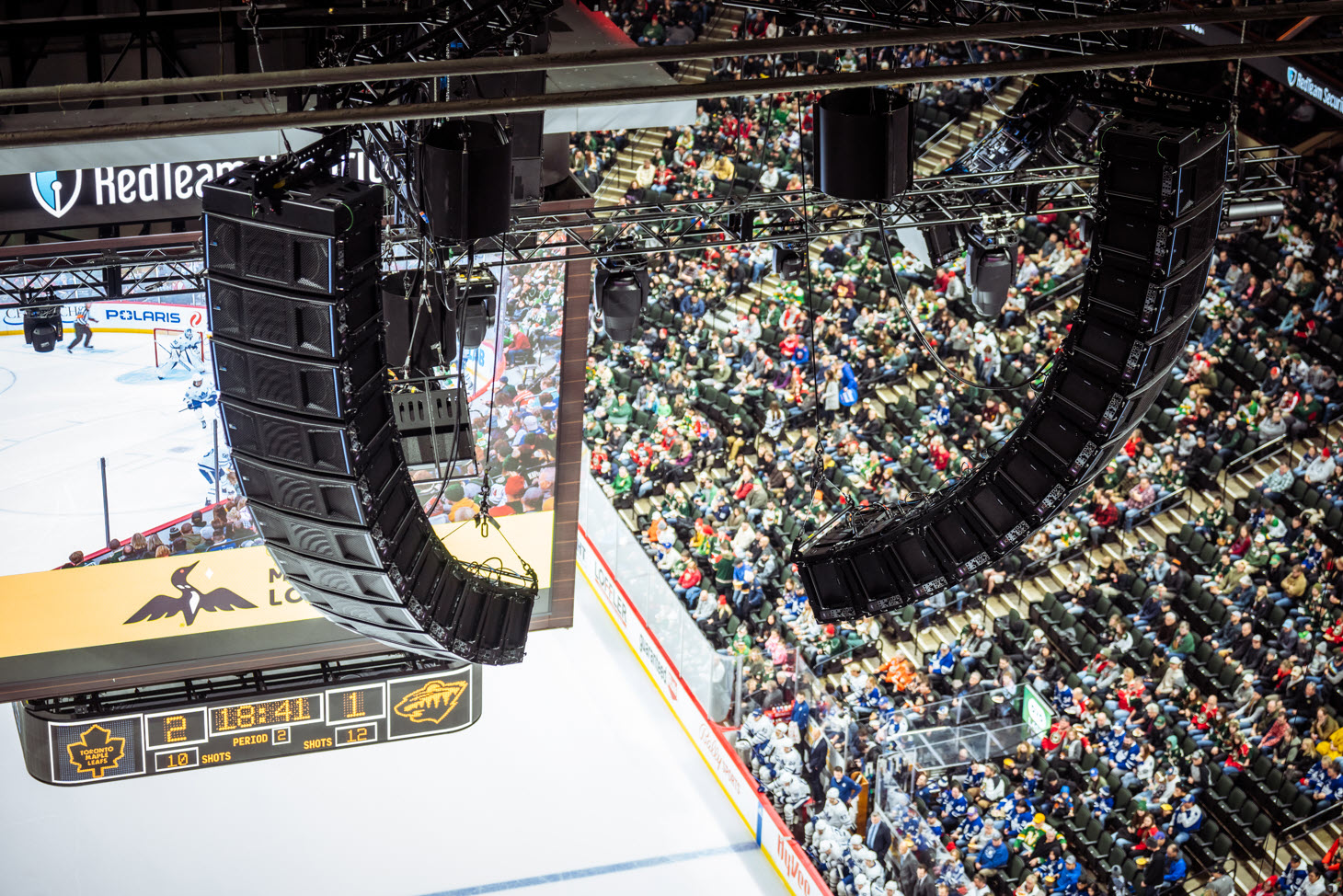 Digital scoreboard and speakers hanging from overhead structure at the Xcel Energy
