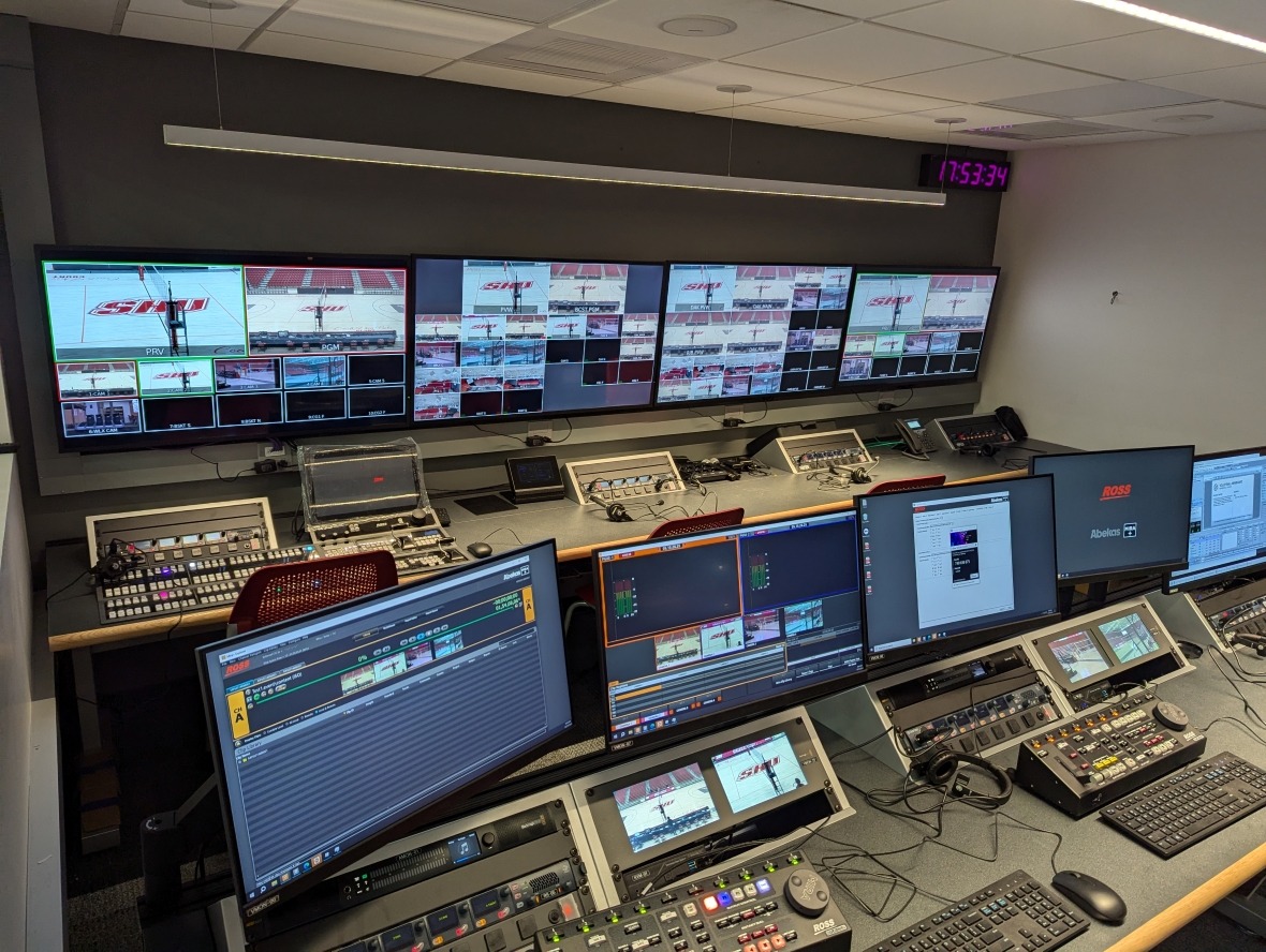 Sports arena control room with rows of screens and various control boards