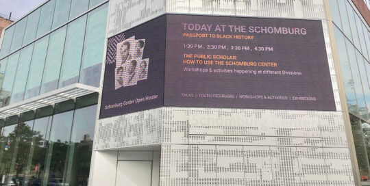 LED display wrapping around the corner of a building. The display is showing content that announces Today at the Schomburg